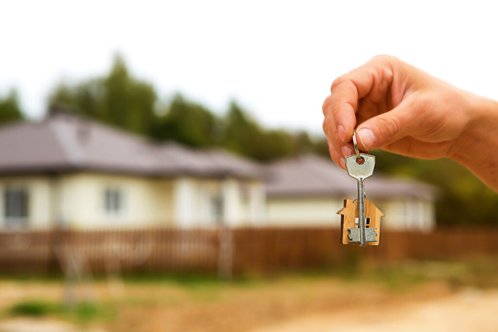 Hand with a key and a wooden key ring-house.